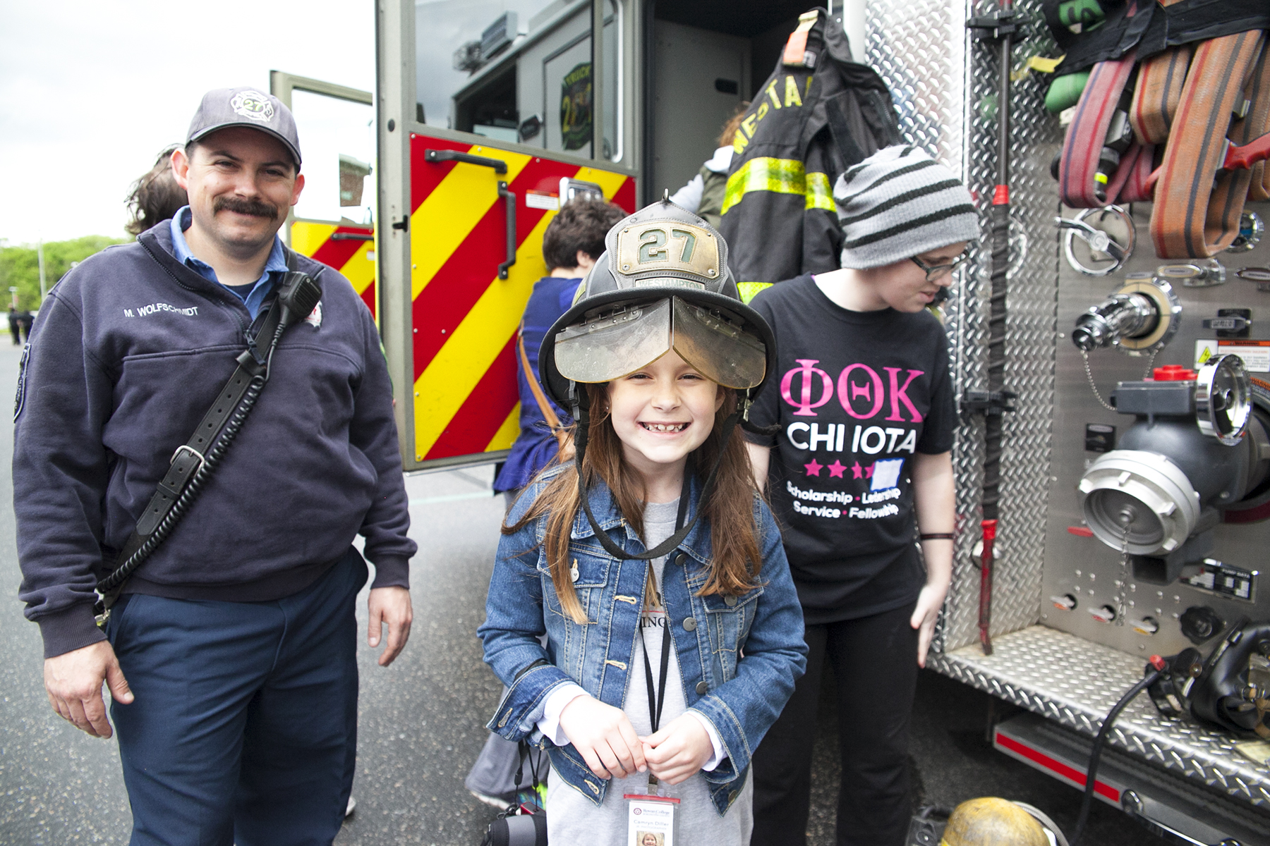 family next to fire truck, young girl wearing a fireman's hat