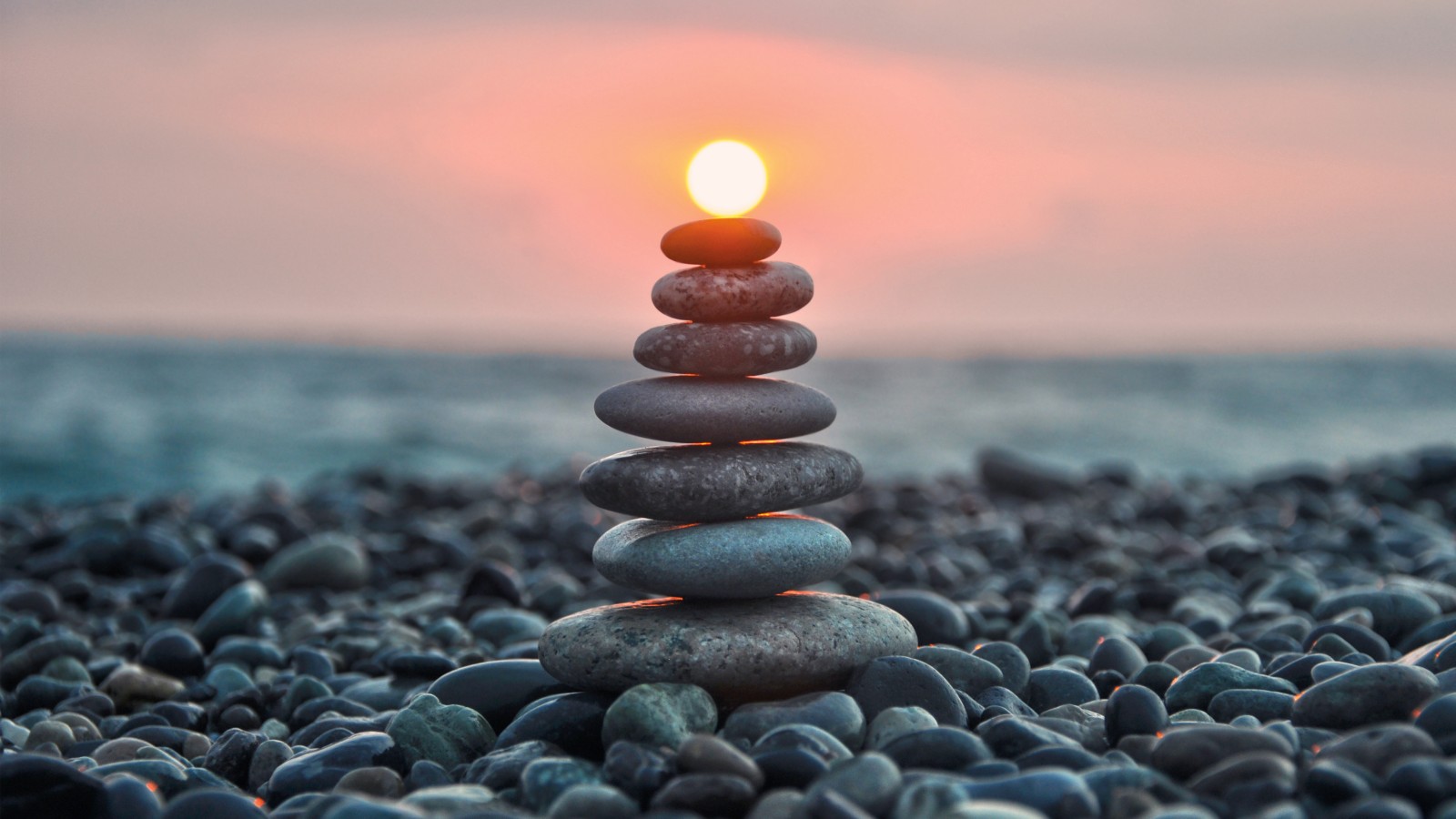 Zen stones stacked on top each with the sun in the background 