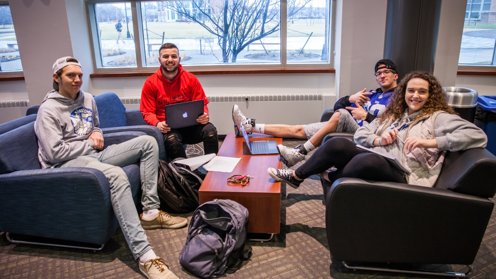 four students sitting on couches smiling 